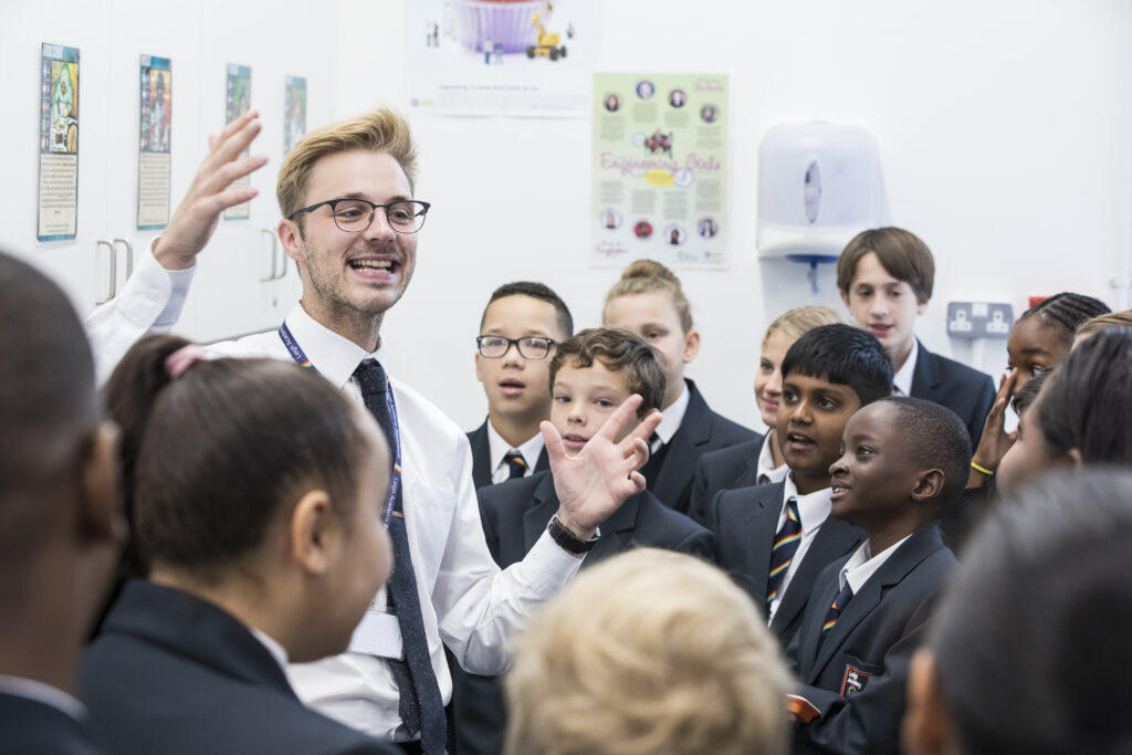 A male staff member is seen talking enthusiastically to students in a group about his subject.